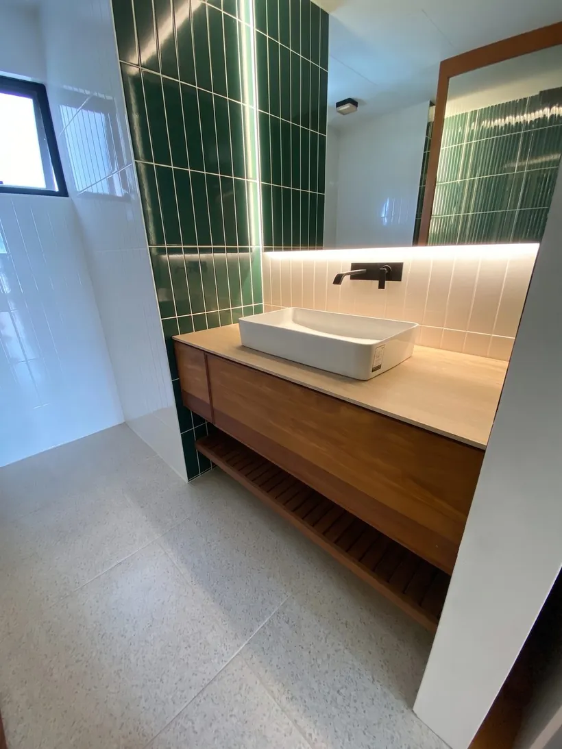 Mueble de lavabo suspendido en madera visto en ángulo, con muro de azulejo verde