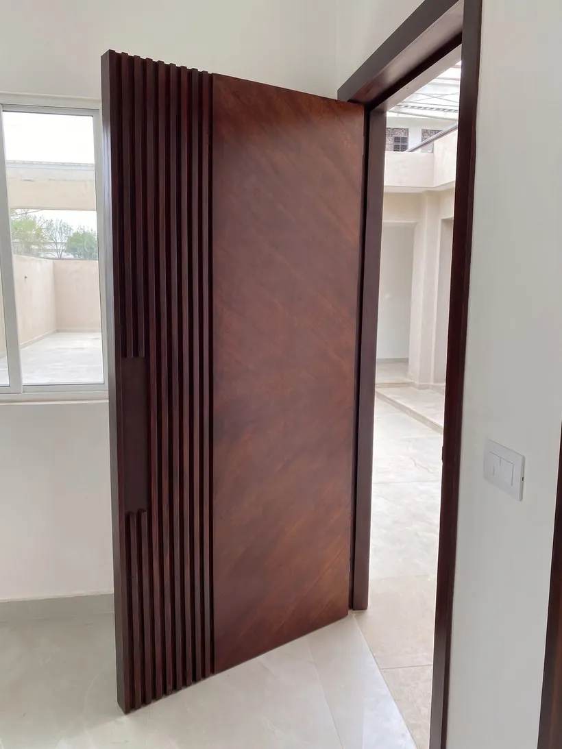 Puerta pivotante de madera abierta, mostrando el canto de tablilla